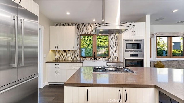 kitchen featuring sink, tasteful backsplash, built in appliances, island exhaust hood, and white cabinets