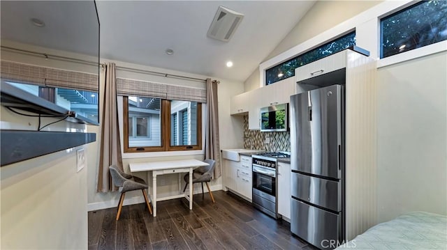 kitchen featuring white cabinetry, lofted ceiling, backsplash, dark hardwood / wood-style flooring, and stainless steel appliances