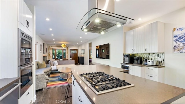 kitchen featuring appliances with stainless steel finishes, dark hardwood / wood-style floors, island range hood, a breakfast bar, and white cabinets