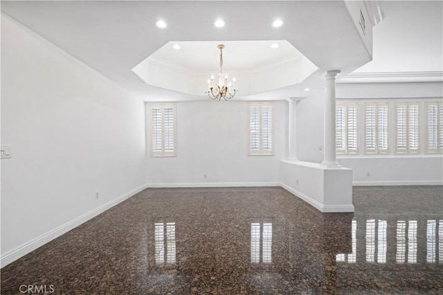 spare room featuring a raised ceiling, ornamental molding, a notable chandelier, and ornate columns