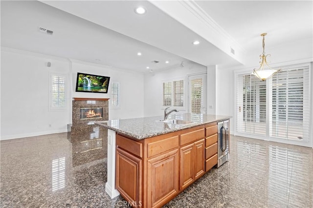 kitchen featuring sink, a premium fireplace, light stone counters, ornamental molding, and an island with sink