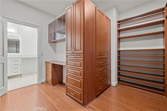 spacious closet with light hardwood / wood-style flooring and built in desk