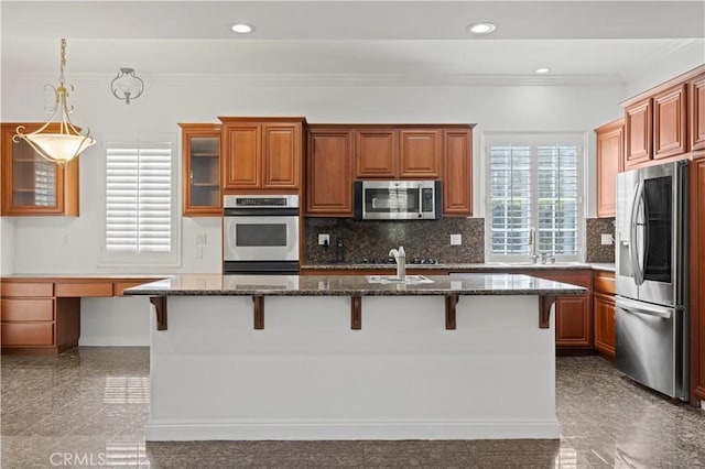 kitchen featuring stainless steel appliances, a kitchen breakfast bar, built in desk, an island with sink, and dark stone counters