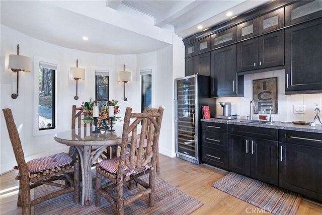 kitchen with sink, wine cooler, light stone counters, light hardwood / wood-style floors, and beamed ceiling