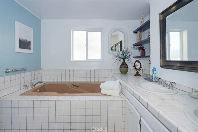 bathroom with vanity, crown molding, and tiled bath