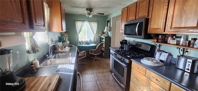 kitchen with sink, ceiling fan, stainless steel appliances, a textured ceiling, and tile patterned floors