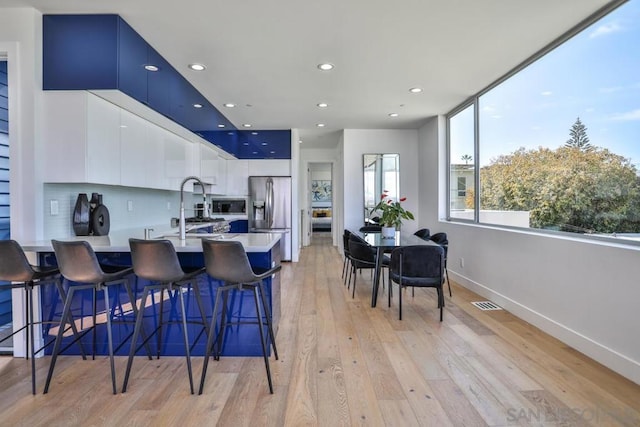 kitchen with stainless steel fridge, a breakfast bar, white cabinetry, backsplash, and built in microwave