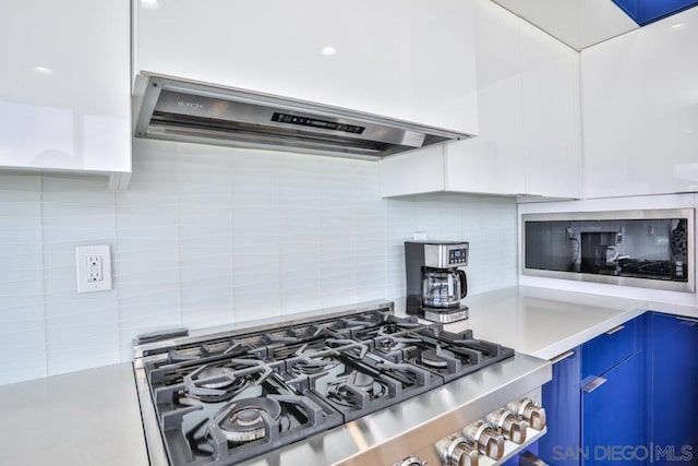 kitchen featuring extractor fan, built in microwave, blue cabinets, decorative backsplash, and cooktop