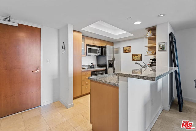 kitchen featuring appliances with stainless steel finishes, a skylight, kitchen peninsula, light tile patterned flooring, and dark stone counters