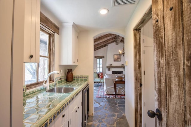 kitchen featuring visible vents, white cabinets, tile countertops, stone finish flooring, and a sink