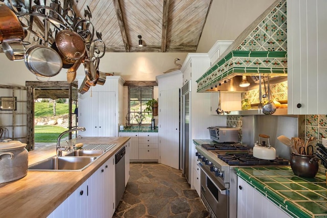 kitchen featuring stainless steel appliances, a sink, white cabinetry, backsplash, and stone finish flooring