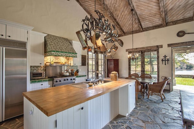 kitchen featuring premium appliances, white cabinets, premium range hood, and wooden counters