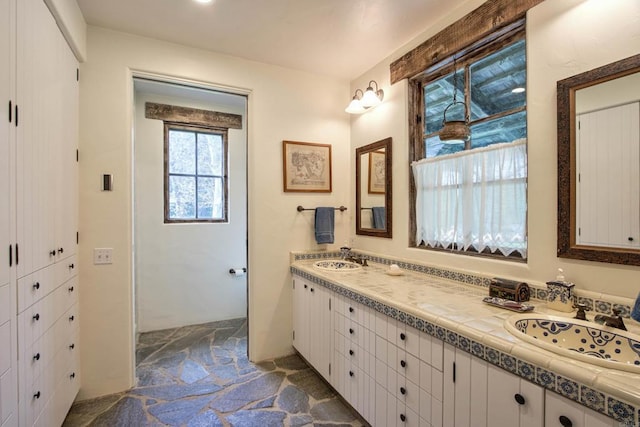 full bath with double vanity, stone flooring, and a sink