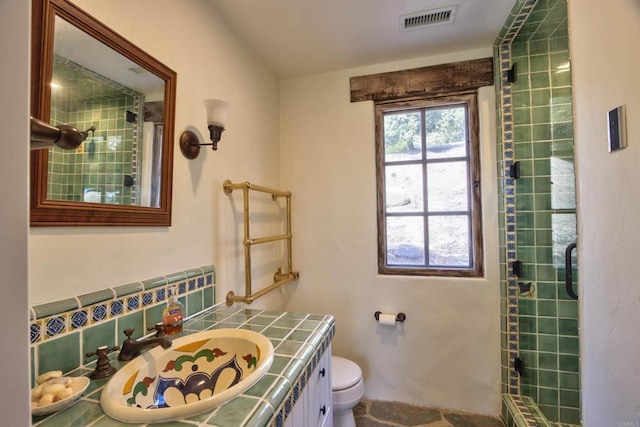 bathroom with visible vents, radiator heating unit, toilet, vanity, and tiled shower