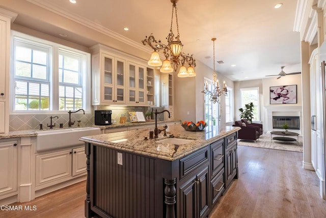 kitchen with pendant lighting, sink, a kitchen island with sink, backsplash, and light hardwood / wood-style floors