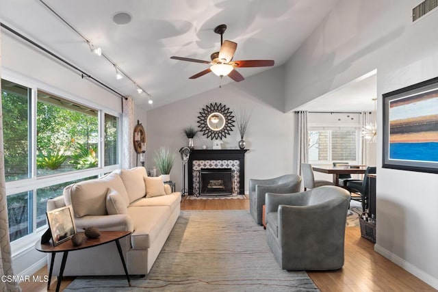 living room featuring lofted ceiling, a tiled fireplace, ceiling fan, light hardwood / wood-style floors, and track lighting