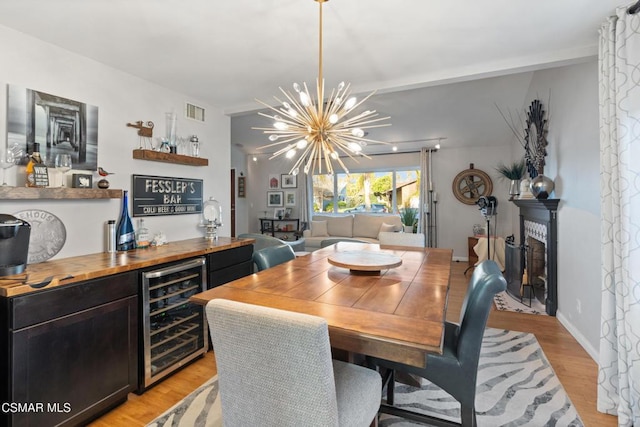 dining room featuring an inviting chandelier, light wood-type flooring, beverage cooler, and bar