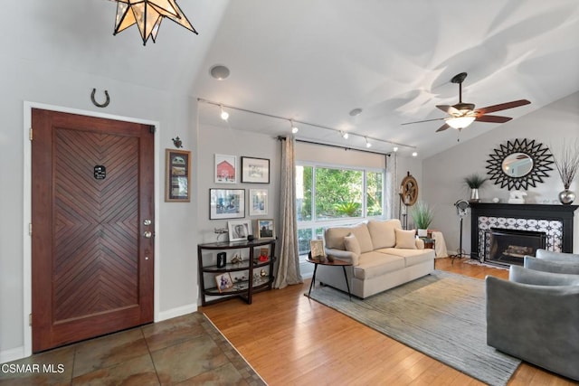 living room featuring lofted ceiling, rail lighting, hardwood / wood-style floors, a fireplace, and ceiling fan with notable chandelier