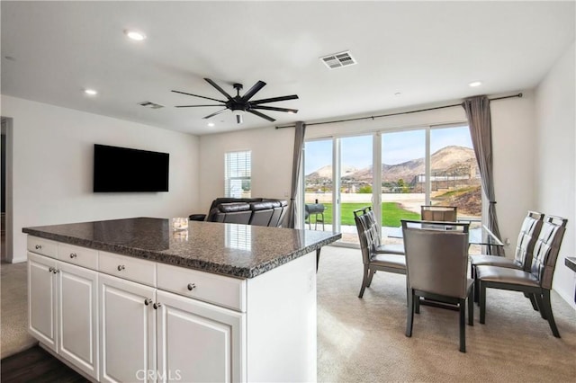 kitchen with ceiling fan, white cabinetry, carpet, a kitchen island, and dark stone counters