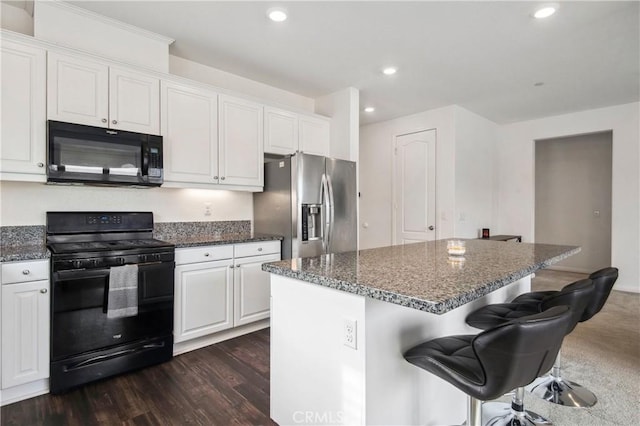 kitchen with a breakfast bar, dark stone countertops, a center island, black appliances, and white cabinets