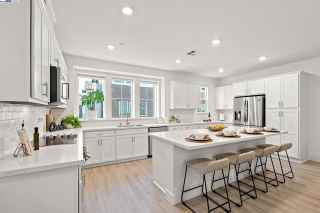 kitchen featuring a kitchen island, appliances with stainless steel finishes, sink, white cabinets, and a kitchen breakfast bar