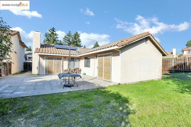 rear view of property with a yard, a patio area, and solar panels