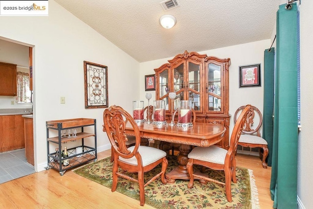 dining space featuring vaulted ceiling, light hardwood / wood-style flooring, and a textured ceiling