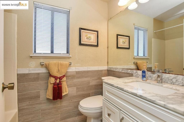 bathroom with vanity, toilet, tile walls, and a wealth of natural light