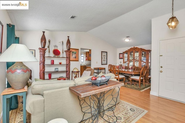 living room featuring sink, vaulted ceiling, a textured ceiling, and light wood-type flooring