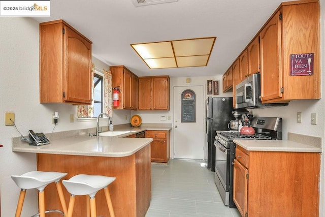 kitchen with a breakfast bar, stainless steel appliances, kitchen peninsula, and sink