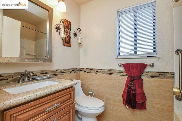 bathroom featuring walk in shower, vanity, toilet, and tile walls