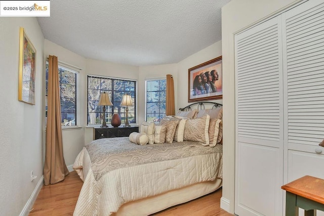 bedroom with a closet, a textured ceiling, and light hardwood / wood-style flooring