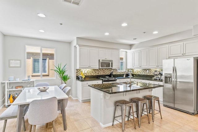 kitchen with white cabinetry, sink, dark stone countertops, a kitchen island with sink, and stainless steel appliances