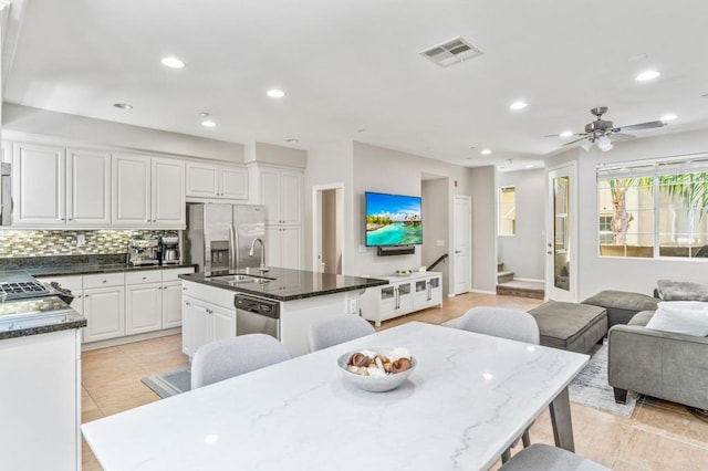 kitchen with sink, white cabinetry, a center island with sink, appliances with stainless steel finishes, and dark stone counters