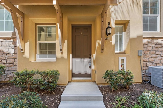 entrance to property featuring stone siding, central AC, and stucco siding