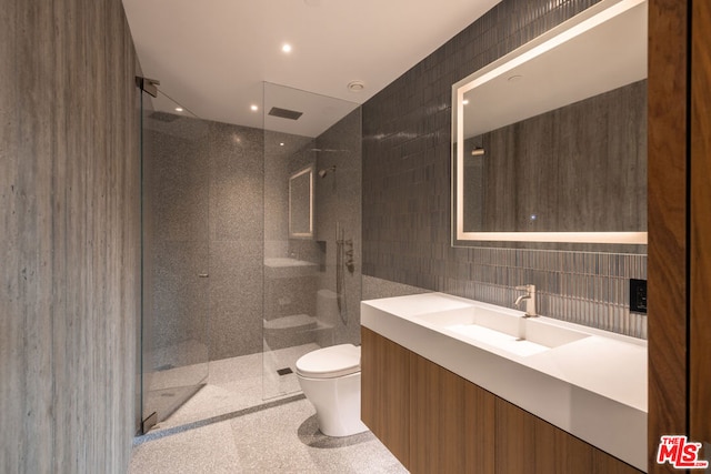 bathroom with tile walls, vanity, toilet, and tiled shower