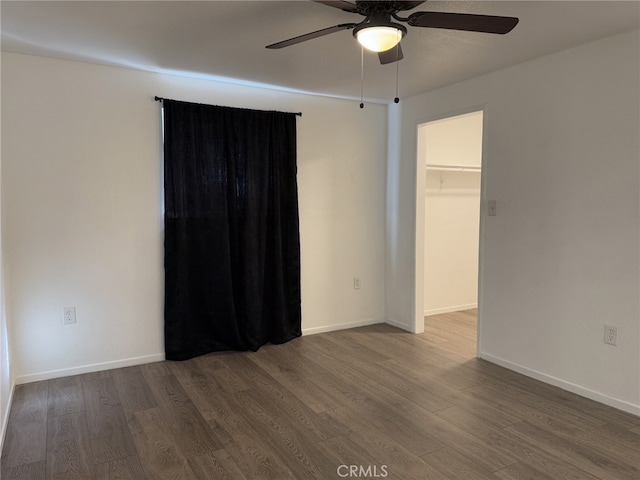 unfurnished bedroom with a ceiling fan, a spacious closet, baseboards, and wood finished floors