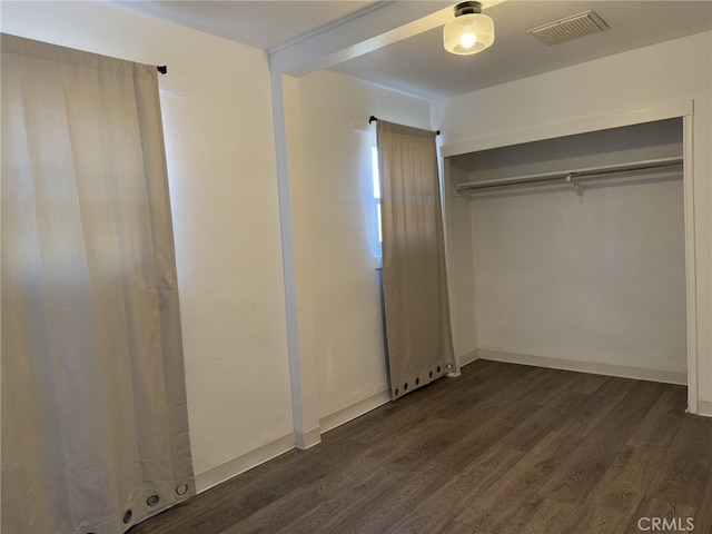 unfurnished bedroom featuring dark wood-style flooring, a closet, visible vents, and baseboards