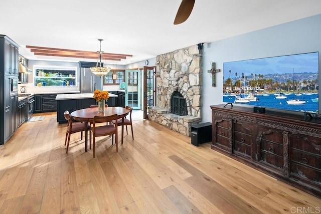 dining space featuring a fireplace, light wood-style flooring, and ceiling fan with notable chandelier