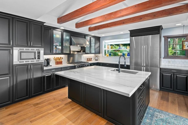 kitchen featuring wall chimney exhaust hood, appliances with stainless steel finishes, a sink, and dark cabinetry