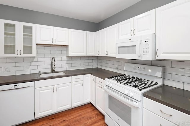 kitchen with dark countertops, white appliances, backsplash, and a sink