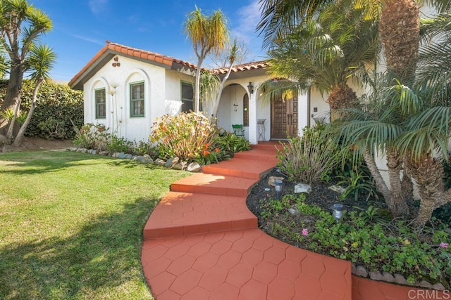 mediterranean / spanish-style house with a front lawn, a tile roof, and stucco siding