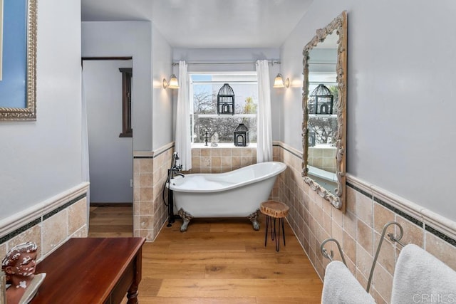 bathroom featuring a freestanding bath, a wainscoted wall, wood finished floors, and tile walls