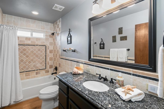 bathroom featuring toilet, vanity, visible vents, tile walls, and shower / tub combo with curtain