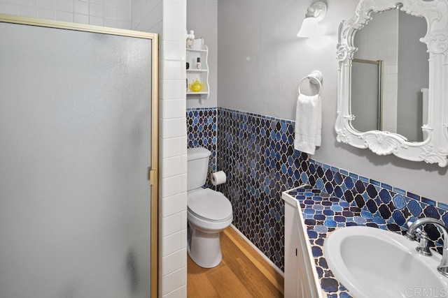 full bath with toilet, a wainscoted wall, wood finished floors, tile walls, and a shower stall