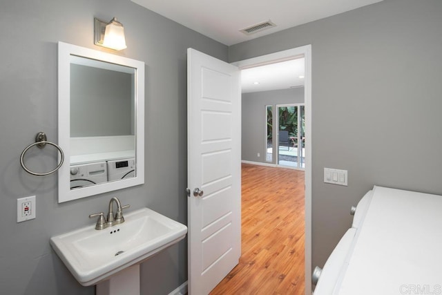 bathroom featuring a sink, wood finished floors, washing machine and clothes dryer, and visible vents