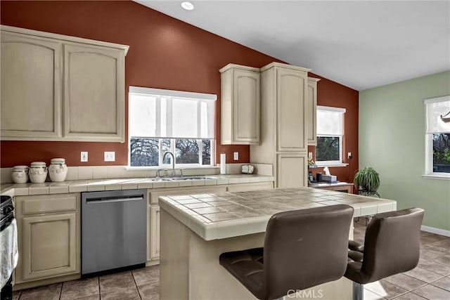 kitchen with light tile patterned floors, tile countertops, lofted ceiling, stainless steel dishwasher, and a sink