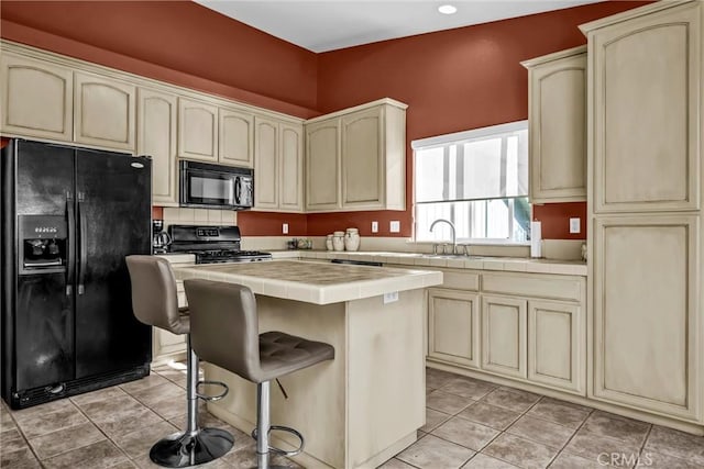 kitchen with black appliances, cream cabinets, and tile counters