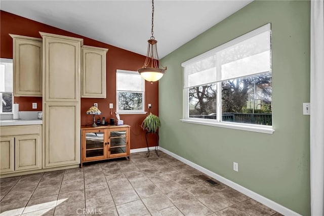 interior space featuring visible vents, baseboards, lofted ceiling, decorative light fixtures, and cream cabinets