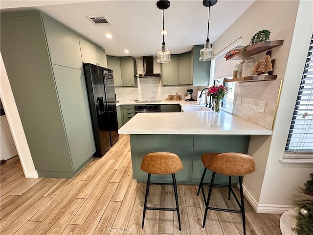 kitchen featuring sink, a breakfast bar, black appliances, wall chimney exhaust hood, and kitchen peninsula